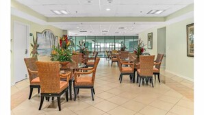 Un vaste espace dédié à la salle à manger, avec des chaises et des tables en osier, entouré de plantes en pot et agrémenté d’œuvres d’art encadrées aux murs.