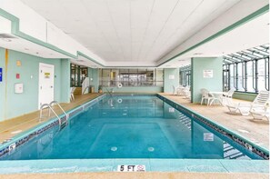 En indendørs swimmingpool med en dybde på 1,5 meter, omgivet af liggestole og et glasparti.