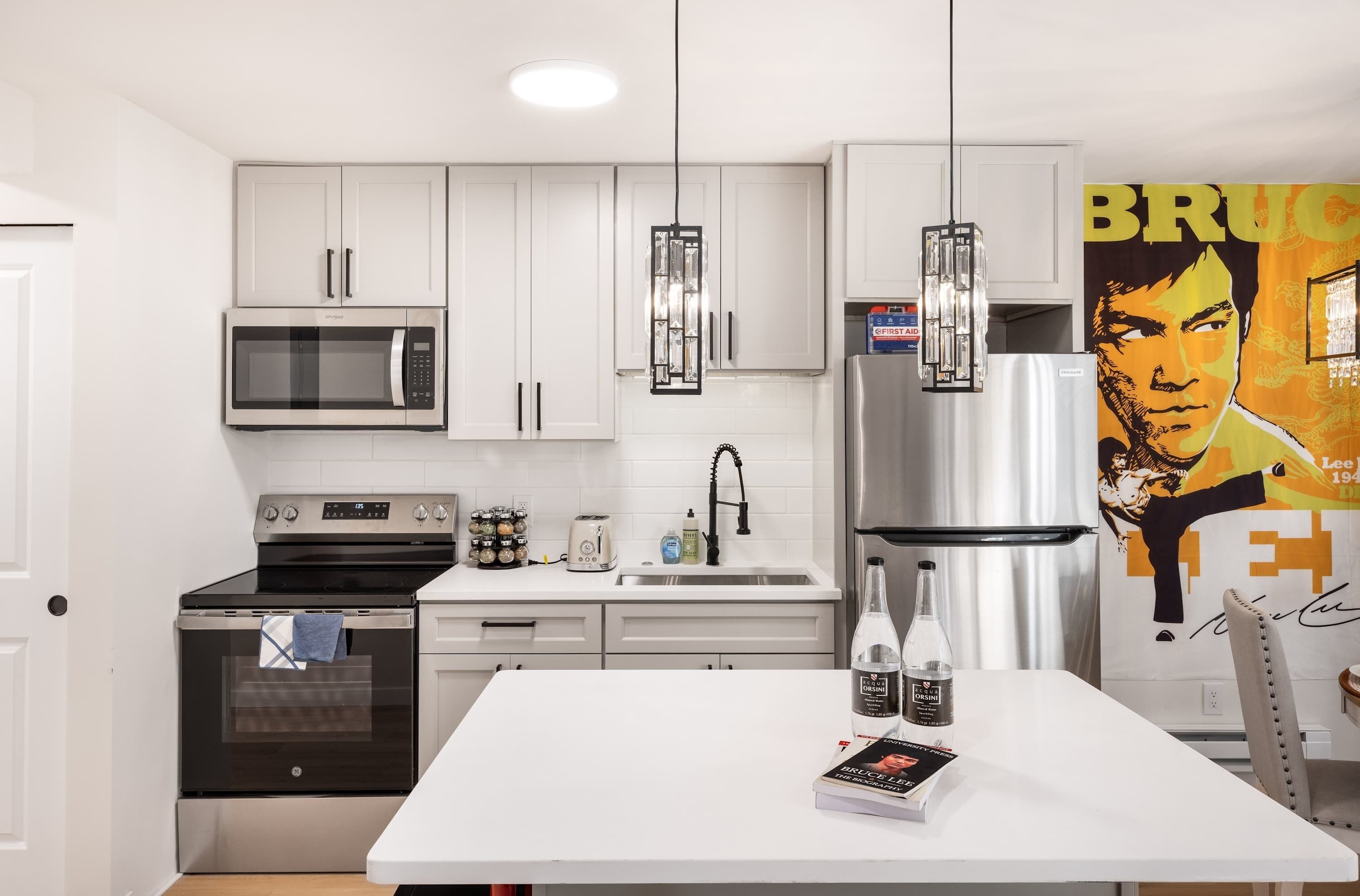 A modern kitchen with white cabinets, stainless steel appliances, and a central island with a book and bottles.
