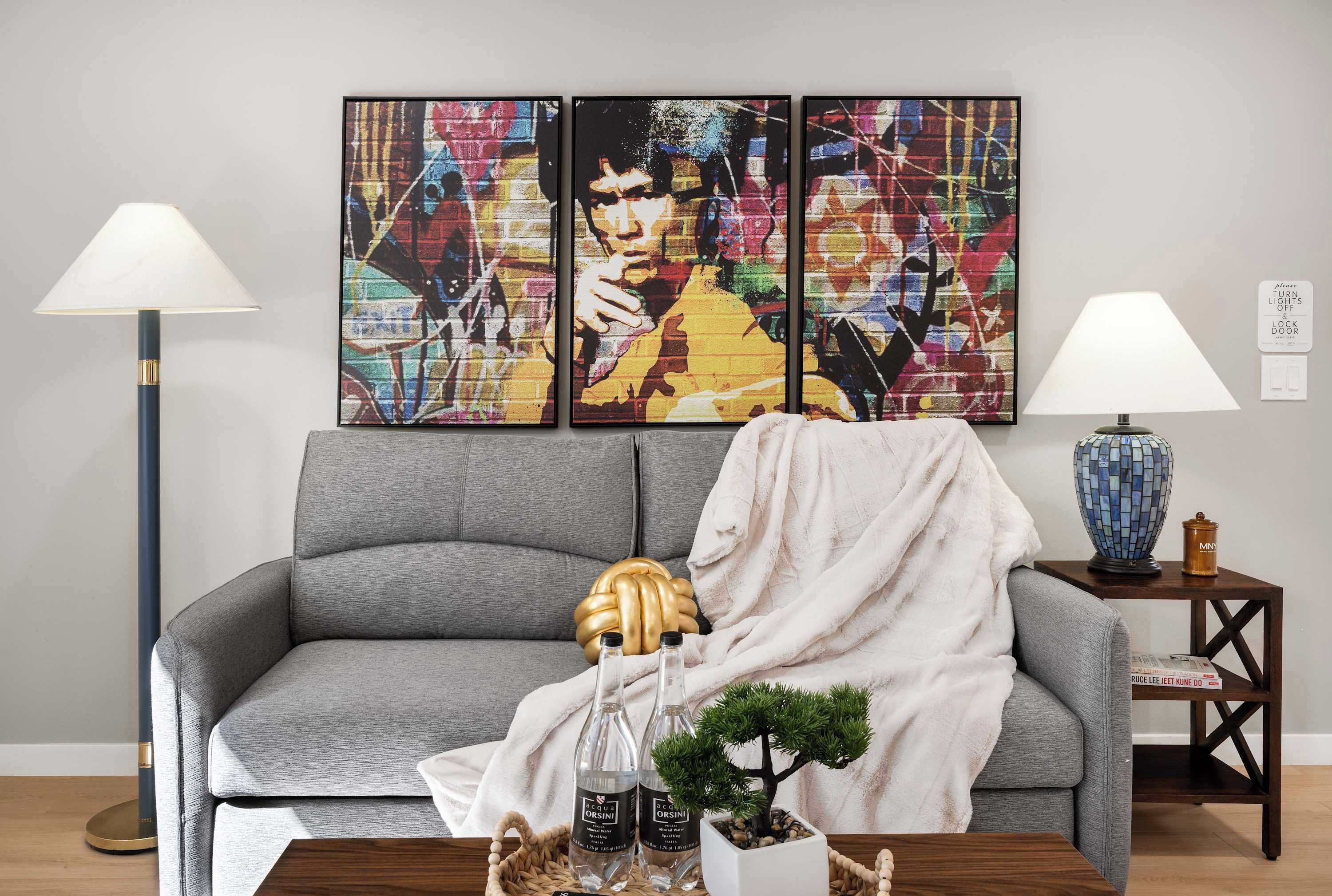 En stue med en grå sofa, et lille sofabord med en blå vase og en gulvlampe.