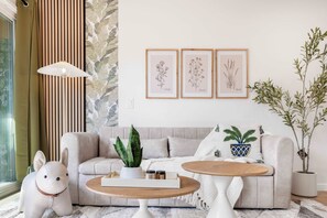 A cozy living room with a sofa, two side tables, a decorative lamp, a potted plant, and framed botanical illustrations on the wall.