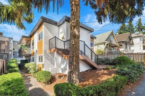 A modern residential building with a white exterior, a wooden deck, and a staircase leading to a balcony.