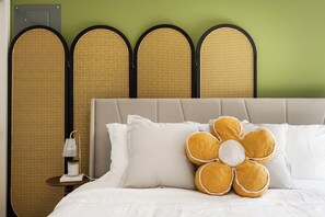 A bed with white bedding, a large flower-shaped pillow, and a nightstand with a lamp.