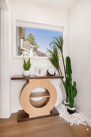 A modern interior with a wooden console table, a round wooden sculpture, a potted plant, a cactus, and a clock. - Brand New 2BR Condo in Queen Anne, Walk to Space Needle (Seattle)