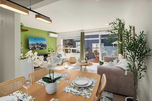 A dining area with a table set for two, a sofa, and a large plant. - Brand New 2BR Condo in Queen Anne, Walk to Space Needle (Seattle)