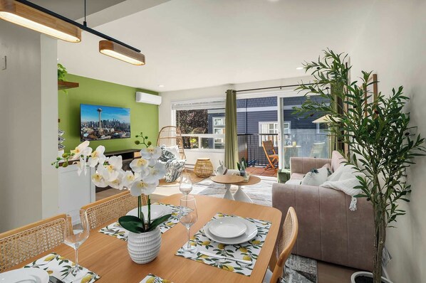 A dining area with a table set for two, a sofa, and a large plant.
