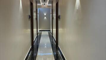 A modern hotel corridor with a reflective black and white tiled floor, recessed lighting, and a straight path leading to a door at the end.