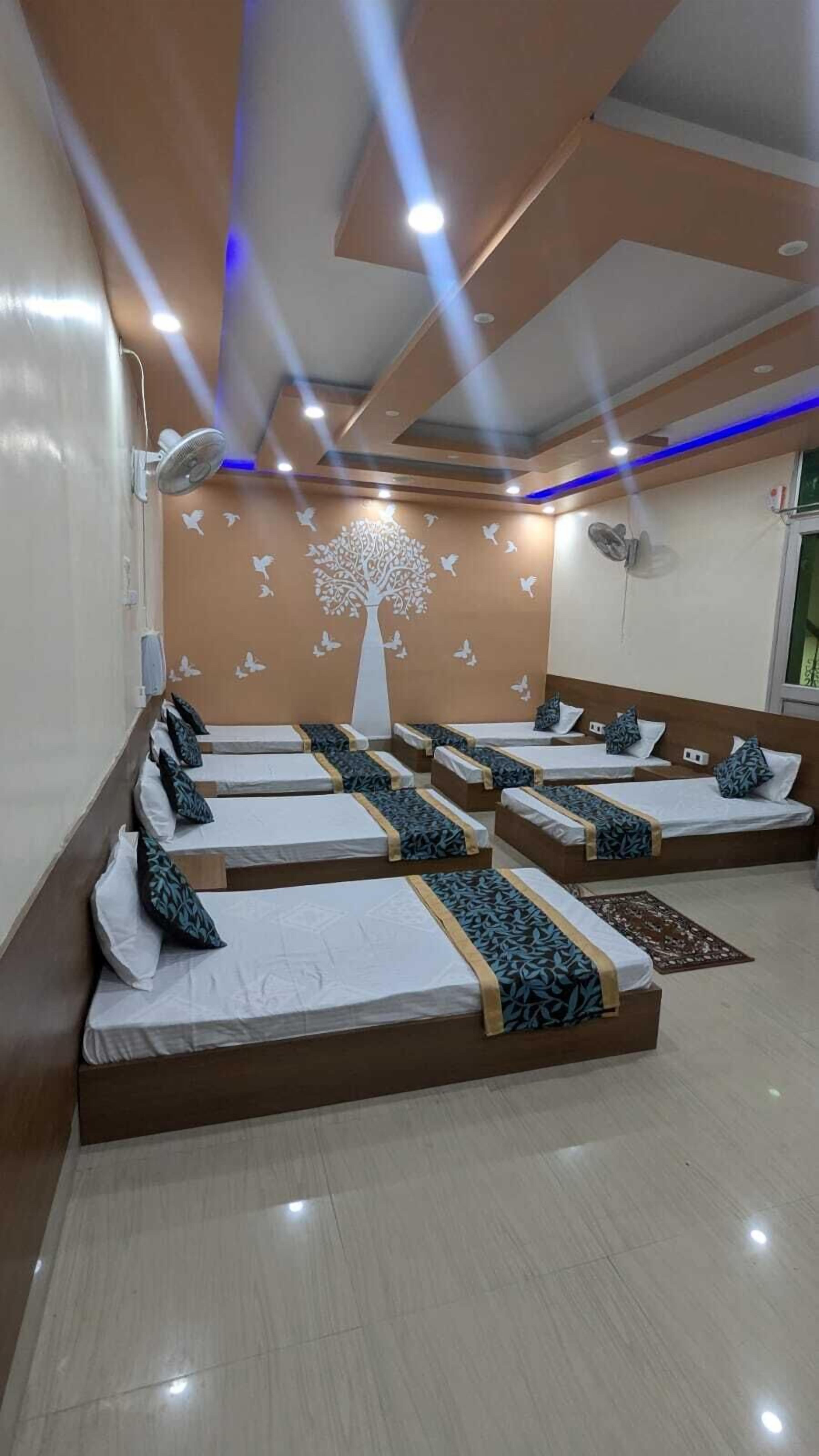 Una stanza con letti disposti in fila, un murale decorativo con un albero e un soffitto con illuminazione a incasso.