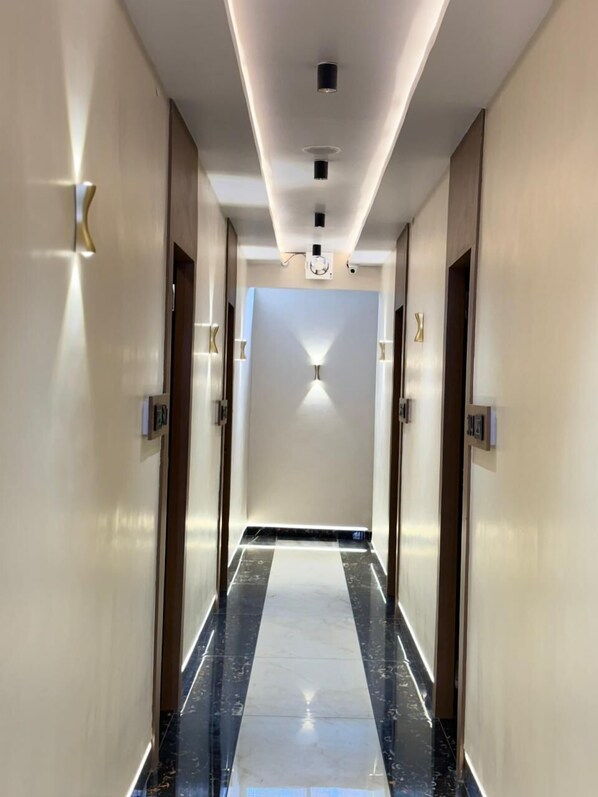 A modern hotel hallway with a marble floor, recessed lighting, and a central light fixture.