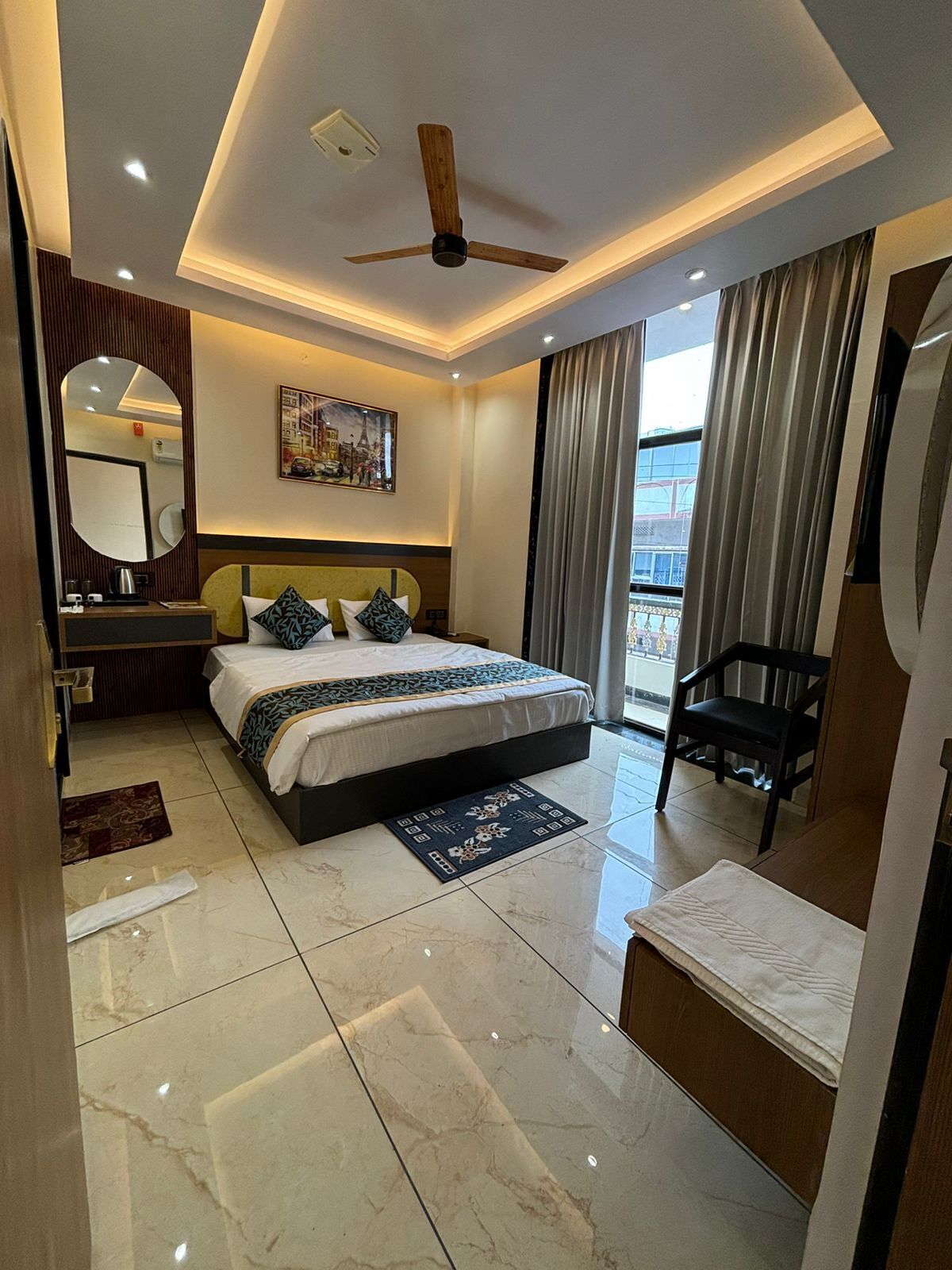 Une chambre d’hôtel moderne avec un grand lit, un ventilateur de plafond, un tableau au mur et une vue sur l’extérieur.