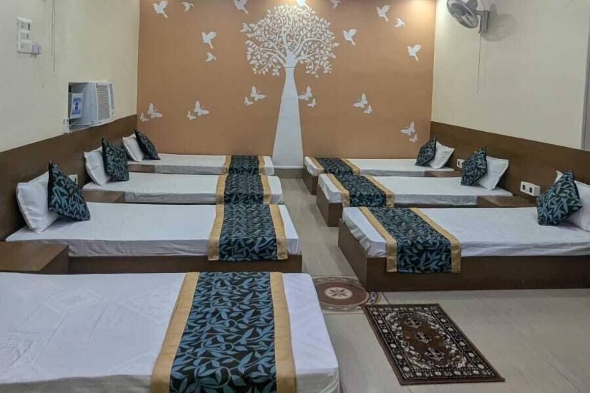 Habitación de hotel con varias camas dispuestas en fila, un mural de un árbol en la pared y un techo con iluminación azul y blanca.