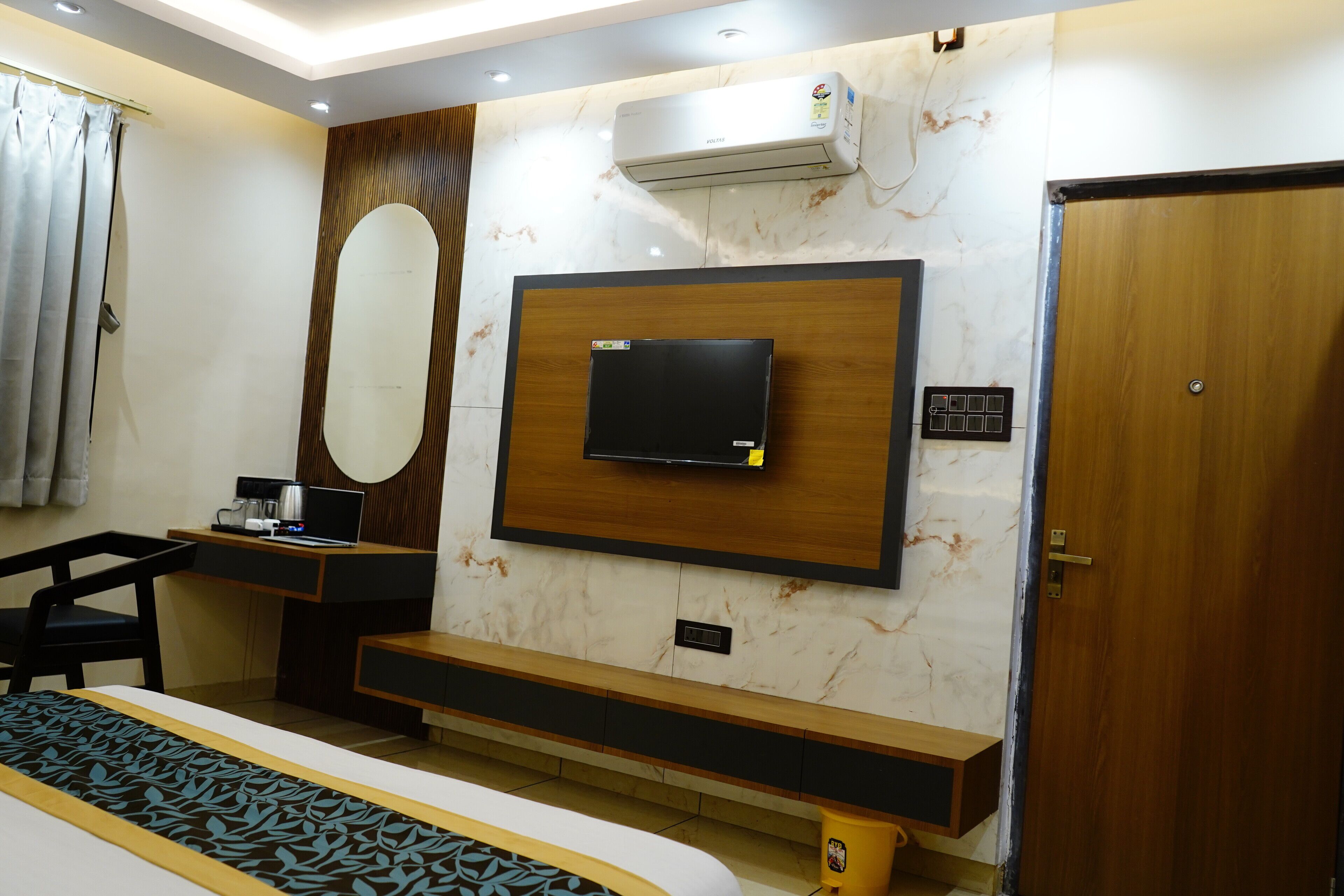 Una habitación de hotel moderna con cama, escritorio con computadora portátil, televisión montada en la pared y unidad de aire acondicionado.