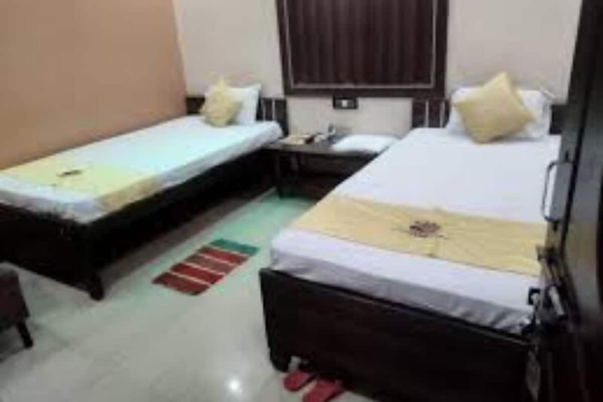 Habitación de hotel con dos camas individuales, una mesita de noche, una pequeña mesa y una ventana con persianas.