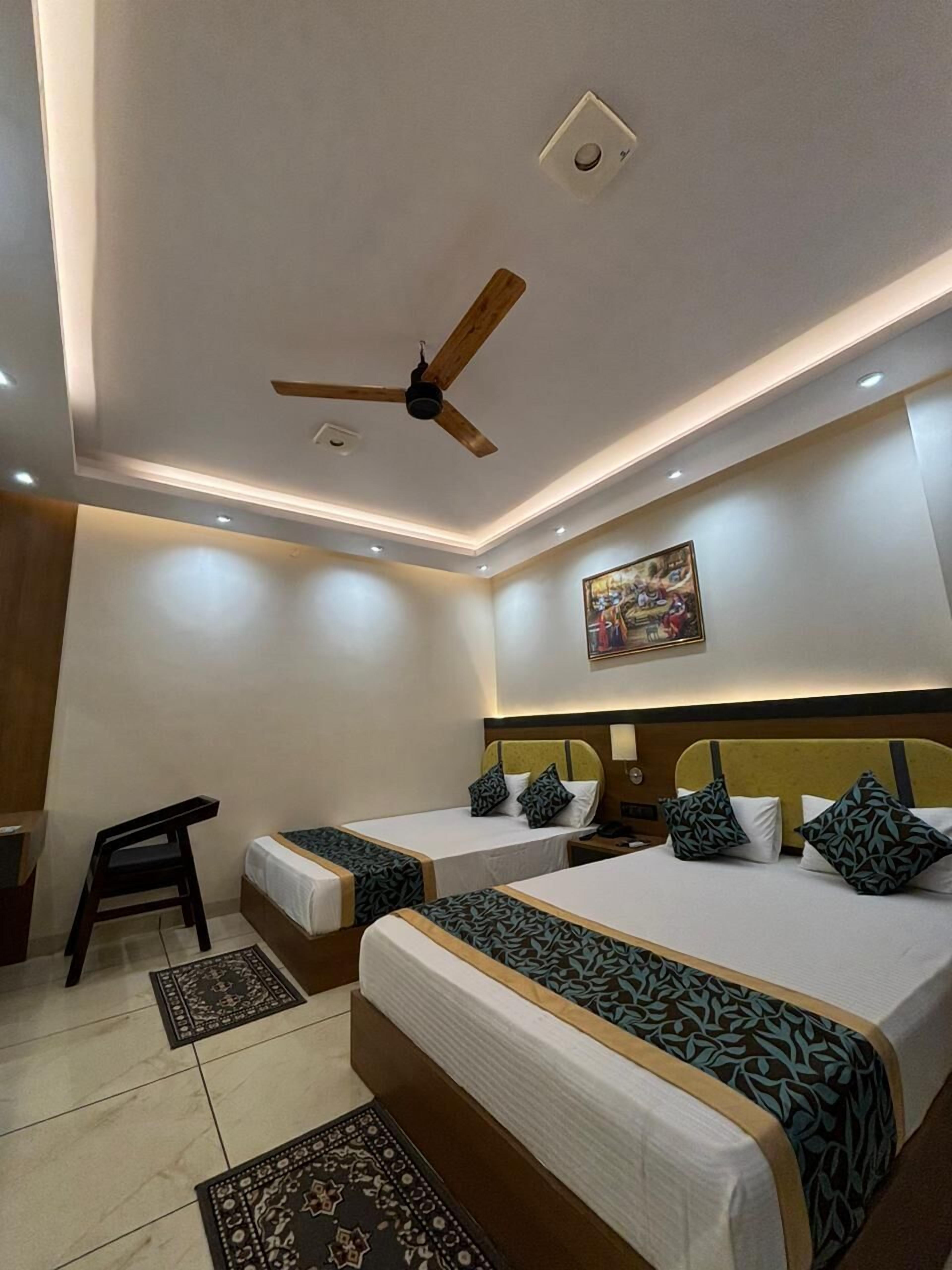 Ein Hotelzimmer mit zwei Betten, einem Deckenventilator, Einbauleuchten, einem Gemälde an der Wand und einem kleinen Schreibtisch mit Stuhl.