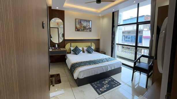 A modern hotel room with a large bed, a ceiling fan, a large window with a view, and a bathroom with a mirror and sink. - Hotel Shakuntla Palace 400 mts to Vishnupad Temple (Gaya)