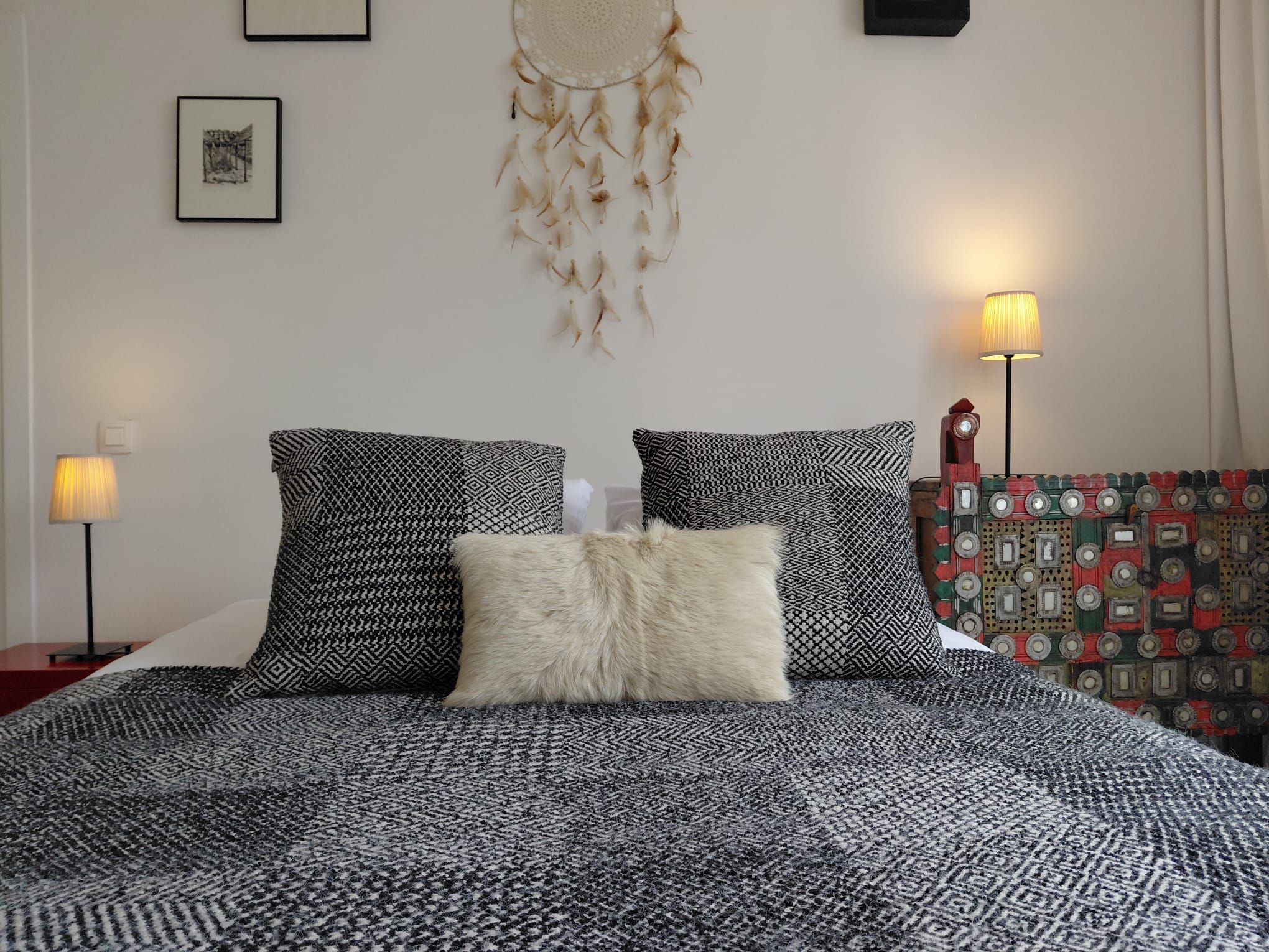 Un lit avec une literie à motifs, un attrape-rêves et deux lampes fixées au mur.