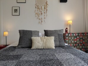 Un lit avec une literie à motifs, un attrape-rêves et deux lampes fixées au mur.