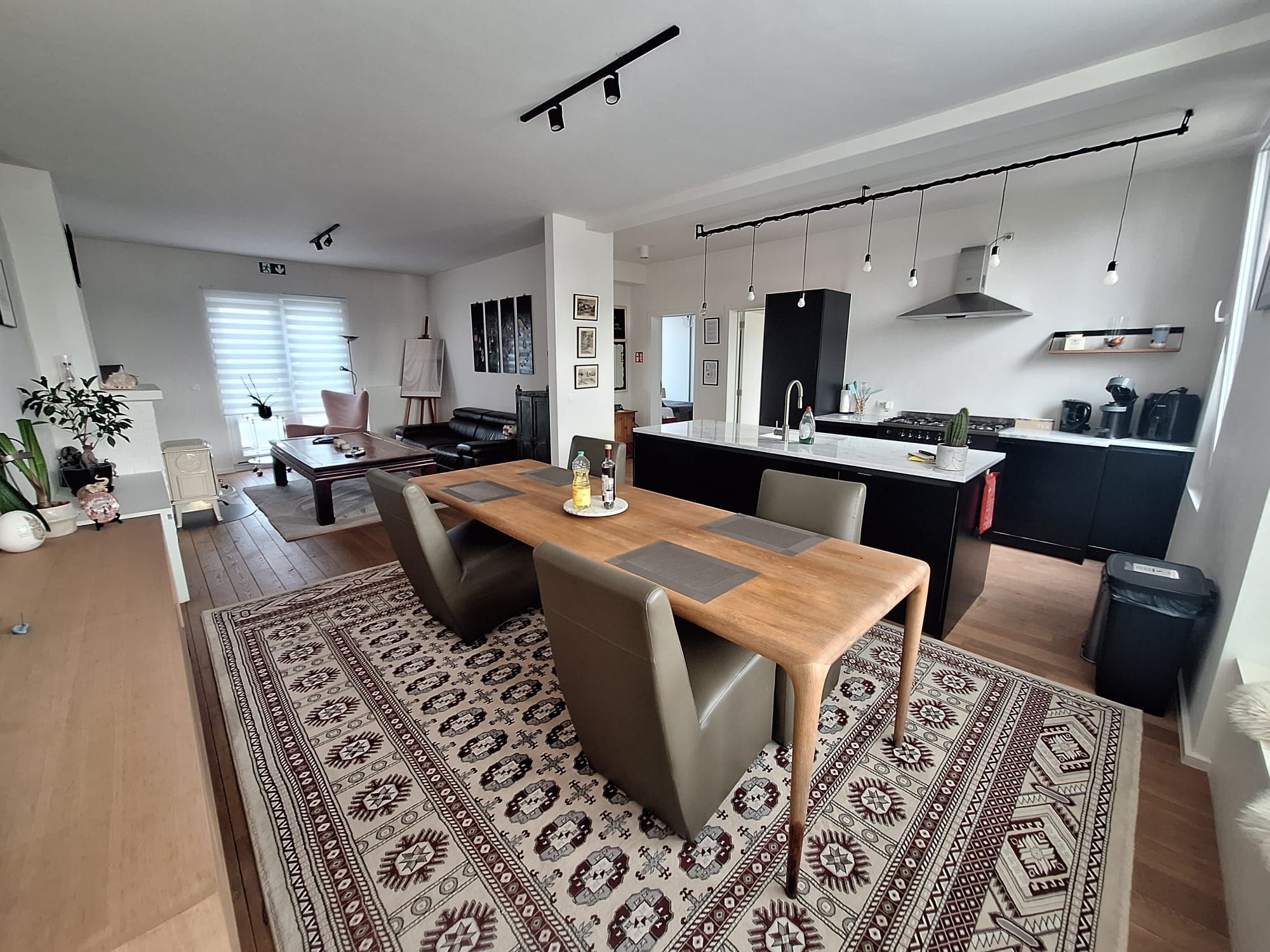 Une cuisine moderne dotée d’un îlot central, un coin repas avec une table et des chaises en bois, et un espace de vie comprenant un canapé et une table basse.