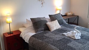 En pænt redt seng med mønstret sengetøj, en drømmefanger og billeder i rammer på væggen.