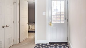 Un couloir avec une porte blanche, un tapis à motifs et un lit à l’arrière-plan.