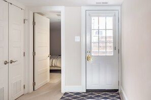 A hallway with a white door, a patterned rug, and a bed in the background.