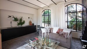 Uma sala de estar moderna com sofá, uma mesa de centro de vidro e uma área de jantar com bancada preta e luminárias pendentes brancas.