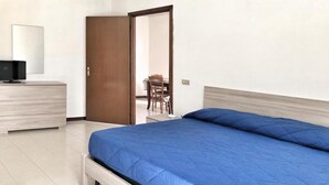 Ein Schlafzimmer mit einem Bett, einem Schminktisch, einem Stuhl und einer Tür zu einem anderen Raum.