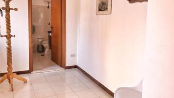 A room with a wooden coat rack, a white chair, a framed picture on the wall, and a bathroom visible through an open door.