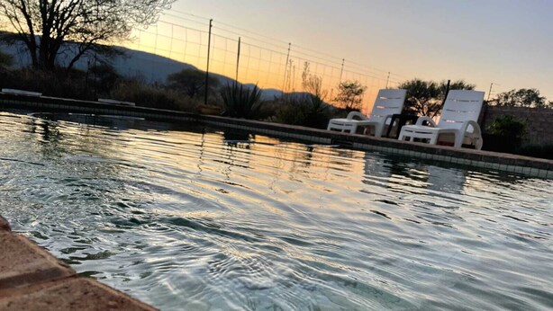 A swimming pool with water reflecting the sky, surrounded by a brick edge and white lounge chairs.