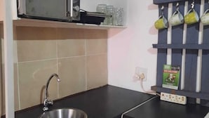 A compact kitchen with a sink, a microwave, and a shelf with jars and a kettle.