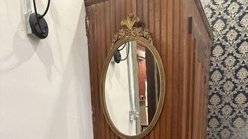 Una stanza d'angolo con un armadio in legno, uno specchio, una poltrona color crema e un piccolo tavolo rotondo con una ciotola.