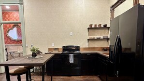 A kitchen with a wooden table, bar stools, a stove, and a refrigerator. - Upscale Western Inn With Historical Distinction and Modern Comfort (Okemah)