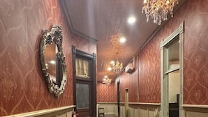A hallway with wooden flooring, a glass table, a chandelier, and a mirror. - Upscale Western Inn With Historical Distinction and Modern Comfort (Okemah)