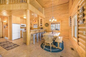 A log cabin interior with a kitchen, dining area, and a loft bedroom.