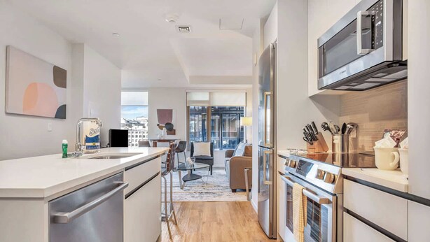 A modern kitchen with stainless steel appliances, a dining area with a glass table, and a view of the city through large windows.
