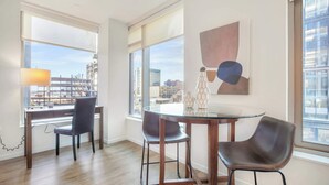 A modern room with a glass table, two chairs, a lamp, and a view of the cityscape through large windows.
