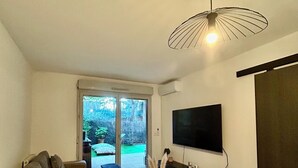 A modern living room with a sofa, a coffee table, a TV, and a sliding glass door leading to a garden.