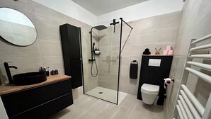 A modern bathroom with a glass-enclosed shower, a black vanity with a round sink, and a white toilet.