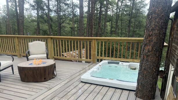 Una terraza de madera con un jacuzzi, una mesa redonda de madera con un brasero y una silla.