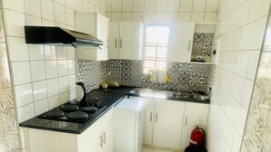 Une cuisine de taille réduite avec des meubles blancs, un plan de travail noir et des carreaux décoratifs sur le mur derrière l’évier.