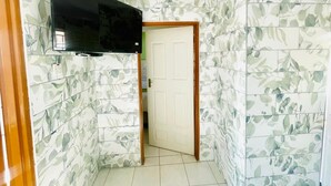 Une pièce dotée d’un téléviseur à écran plat fixé au mur, d’une porte donnant sur une autre pièce et d’un papier peint à motifs.