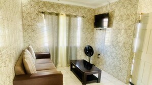 Un salon avec un canapé marron, une petite table, un ventilateur de plafond et un papier peint à motifs.