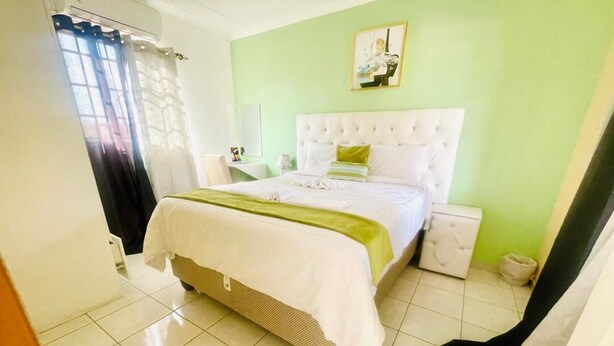 Une chambre à coucher avec un lit, une table de chevet, une commode et une fenêtre avec des rideaux.