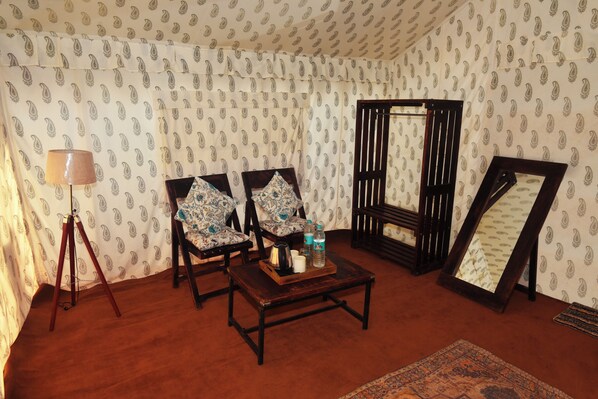 A room with patterned wallpaper, two upholstered chairs, a wooden coffee table, a floor lamp, a mirror, and a rug. - Global Kumbh Village (Karchana)