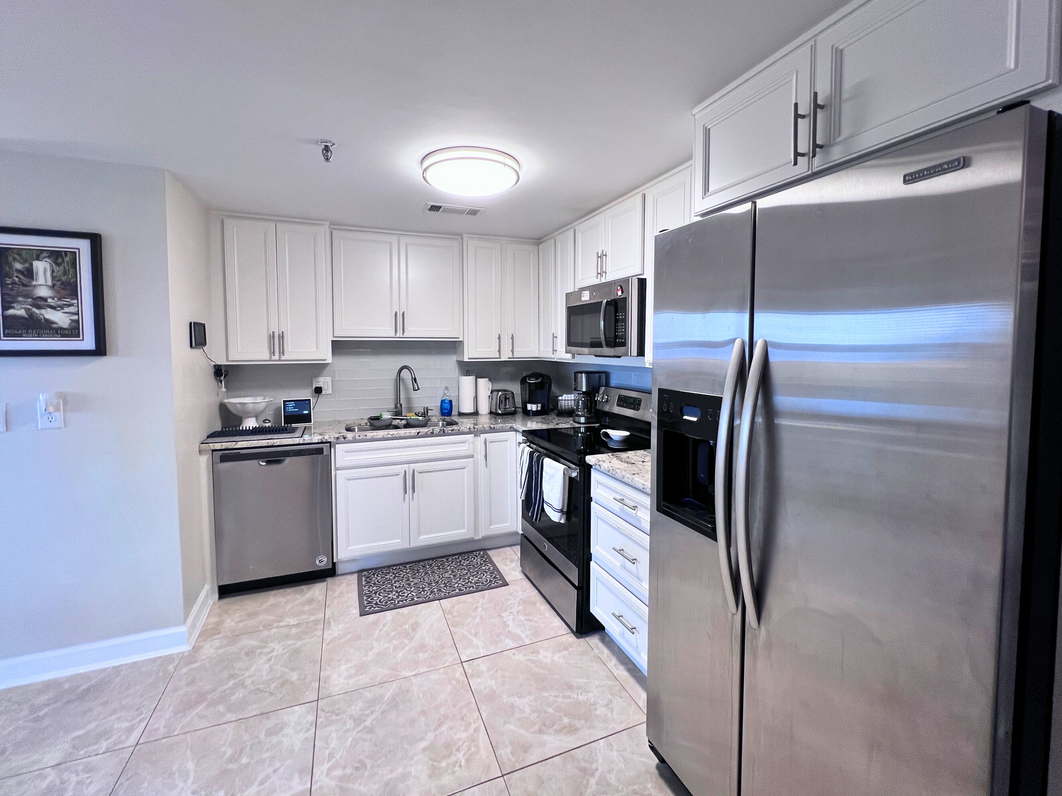A modern kitchen with white cabinets, stainless steel appliances, and a tiled floor.