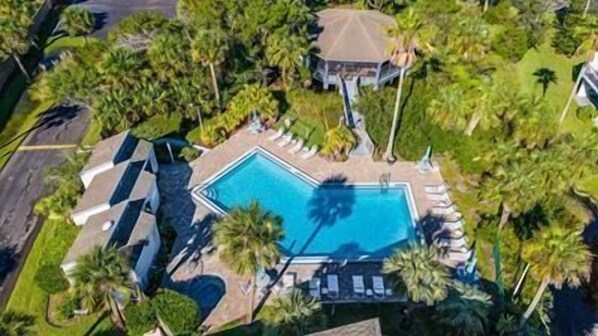 An aerial view of a resort with a central swimming pool, surrounded by palm trees and a gazebo.