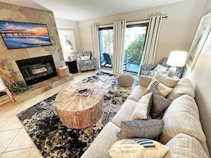A living room with a fireplace, a large flat-screen TV, a sofa set, and a view of the outdoors through the windows. - Sea Winds 78 Oceanfront Beach Community (St. Augustine)