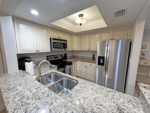 A kitchen with white cabinets, a stainless steel refrigerator, a microwave, a stove, and a double sink. - Sea Winds 78 Oceanfront Beach Community (St. Augustine)