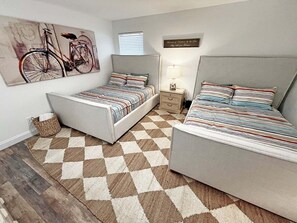 A bedroom with two beds, a checkered rug, a bedside table with a lamp, and a wall-mounted bicycle painting.
