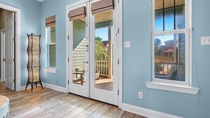 Une pièce aux murs bleu clair, avec un plancher en bois, une grande fenêtre munie de stores, une porte à panneaux de verre et un lampadaire décoratif.